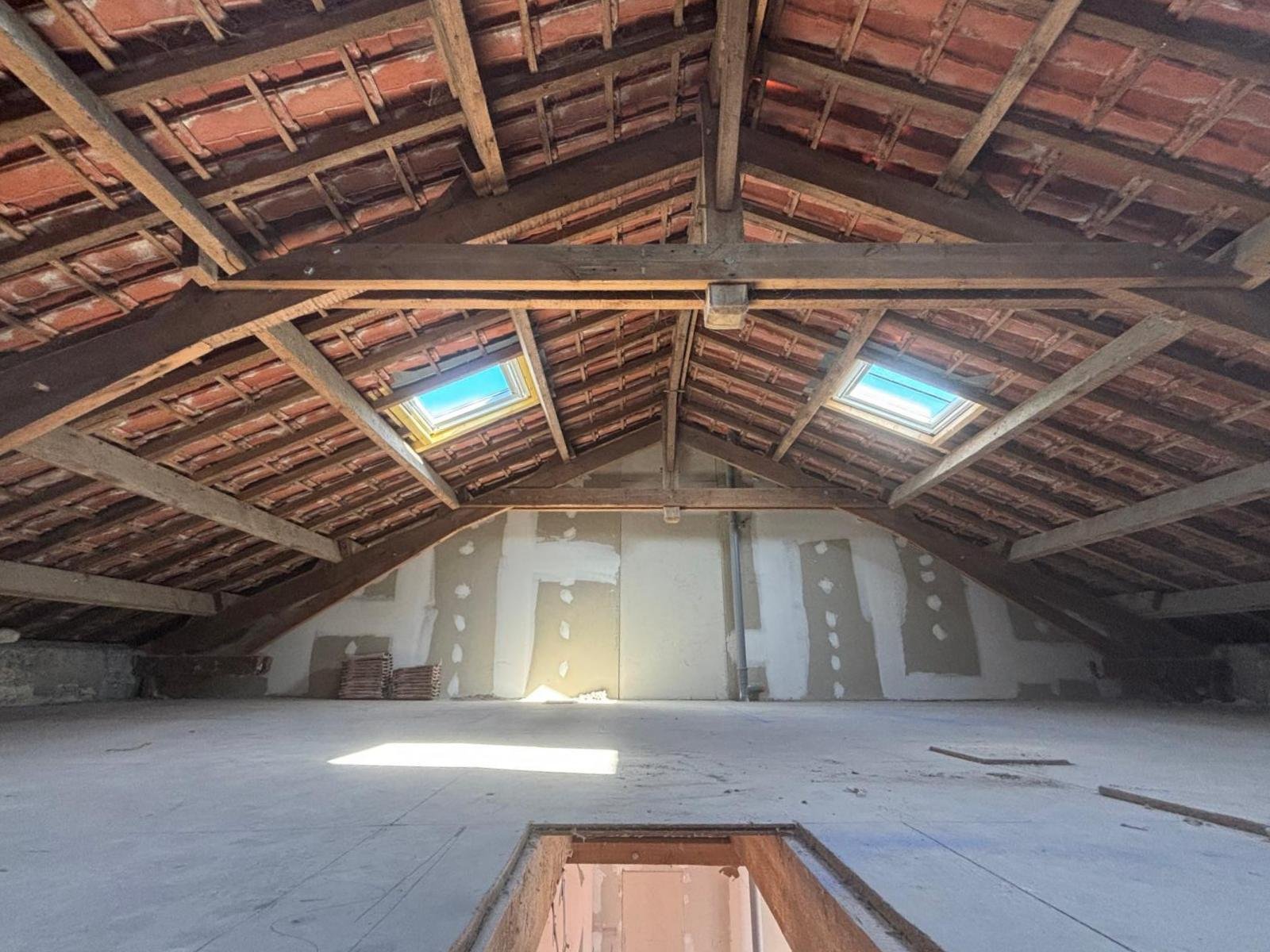 amenagement combles perdus jonzac Grange vide avec un plafond en bois, lucarnes et murs nus.