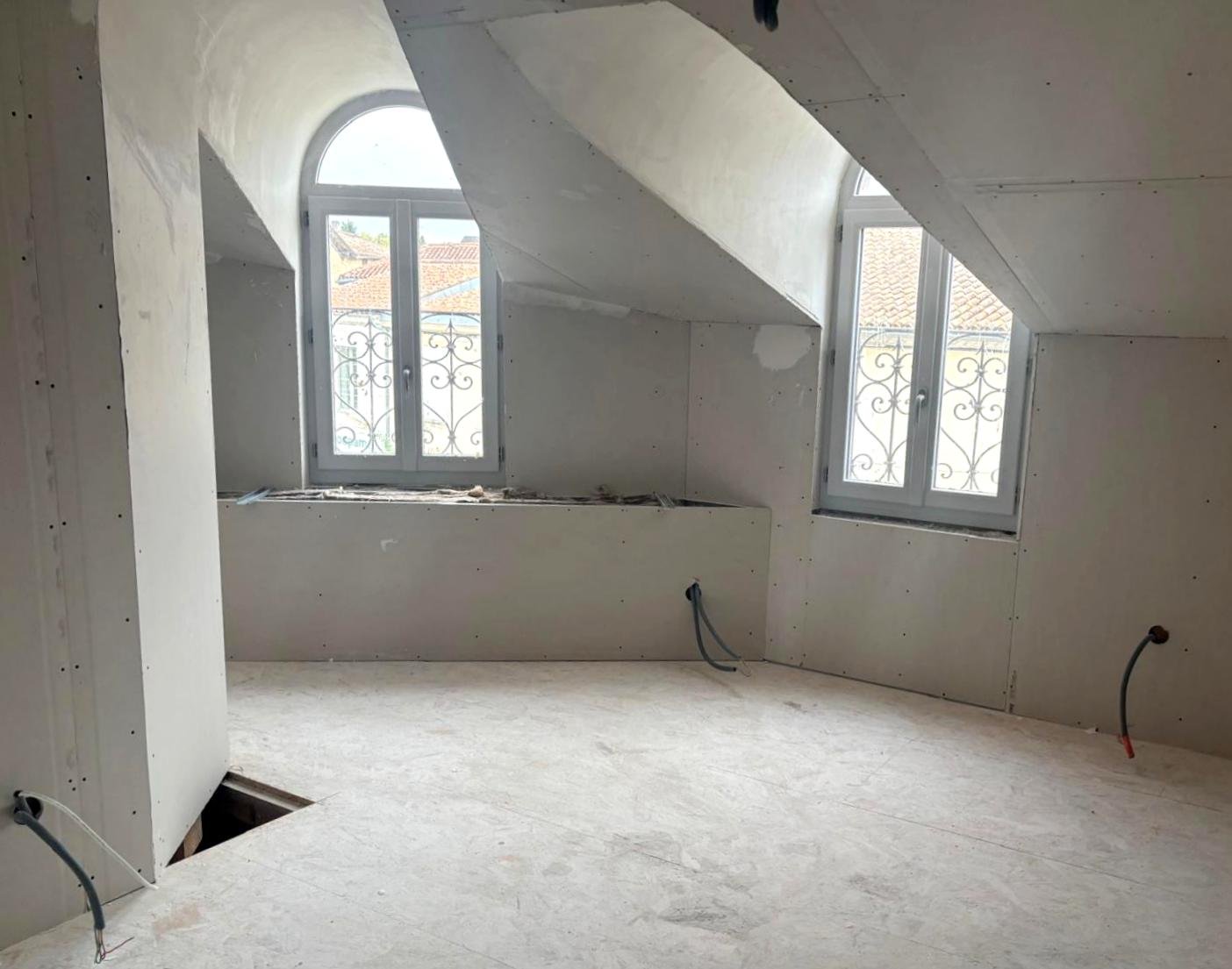 amenagement comble - isolation, electricité et placo Pièce en cours de rénovation avec fenêtres dans les combles, murs en plâtre et câbles électriques.